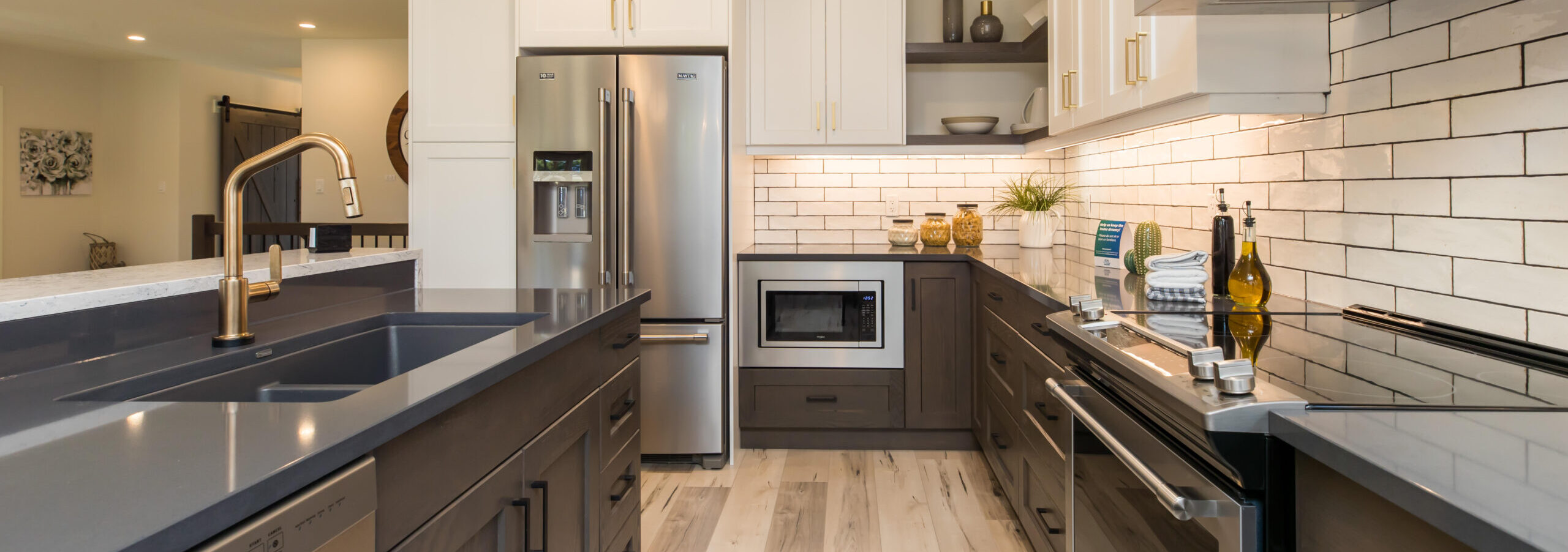 Modern kitchen with dark grey countertop and brushed faucet. White upper cabinets and dark grey lower cabinets with gold and black handles. Design by Sarnia Cabinets.