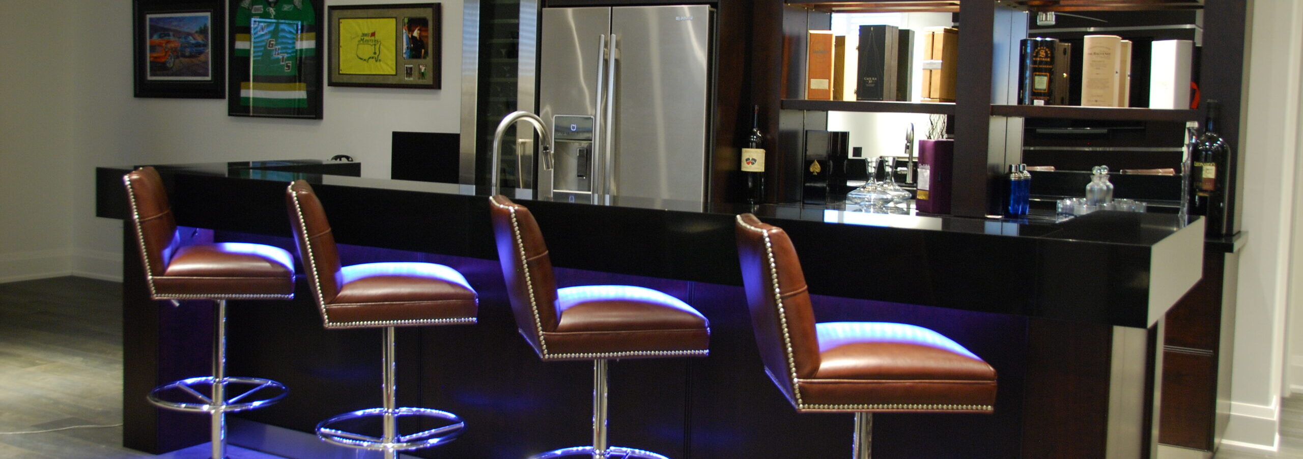 Basement bar with glossy finish on island and shelving. Blue glowing lights under the bar with stools.
